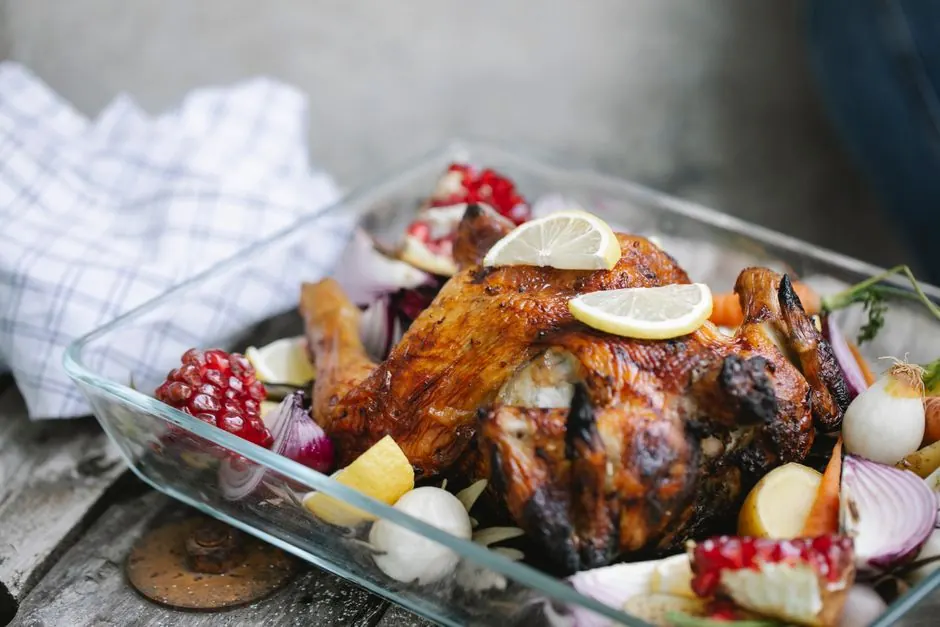 Freshly cooked whole chicken with assorted vegetables and lemons with pomegranate in baking form on kitchen table